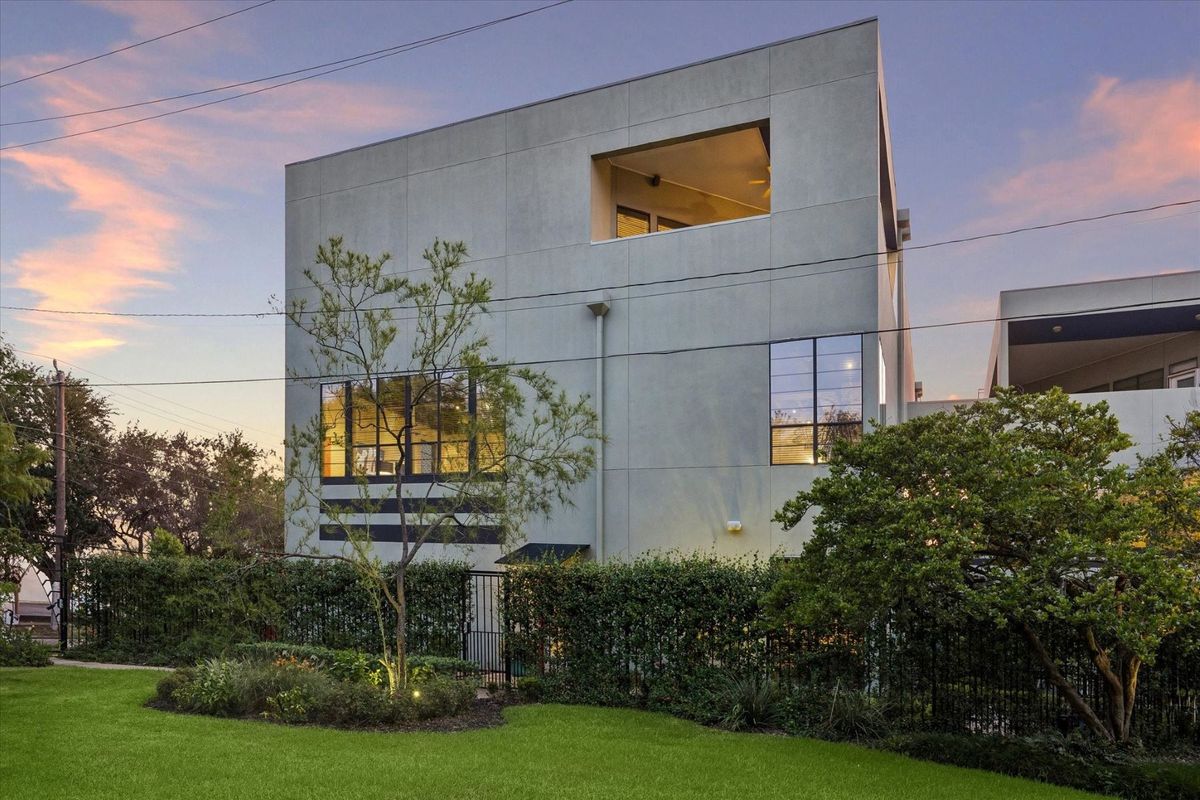 2608 Montrose at dusk, a stucco loft townhome behind a hedge with warm light in the windows